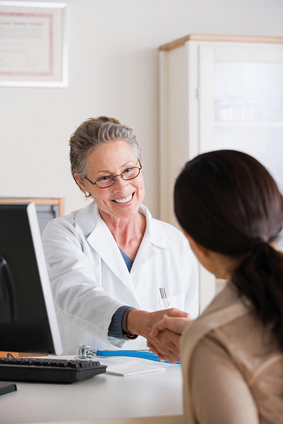 Eine Ärztin sitzt an ihrem Schreibtisch und begrüßt mit einem Handschlag eine Patientin.