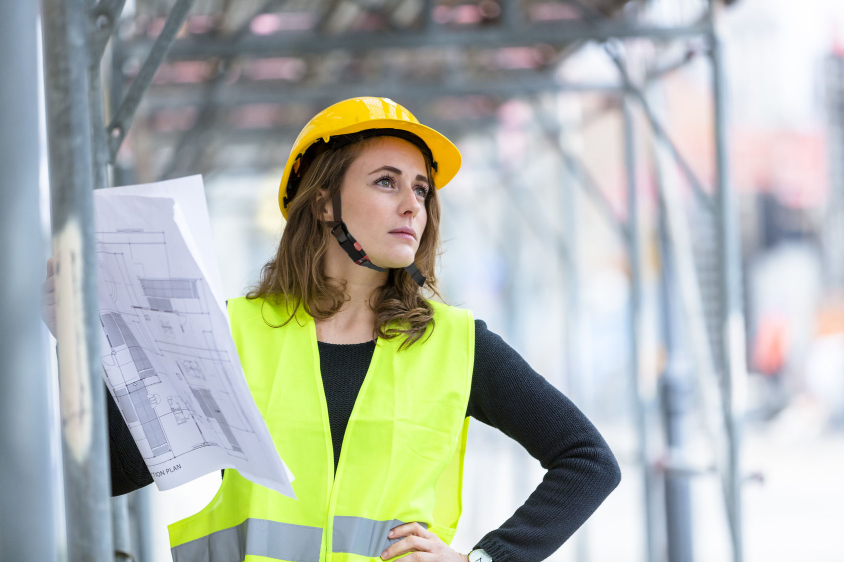 Ein Porträt einer Bauleiterin, die mit persönlicher Schutzausrüstung wie Schutzhelm und Warnweste auf einer Baustelle steht.