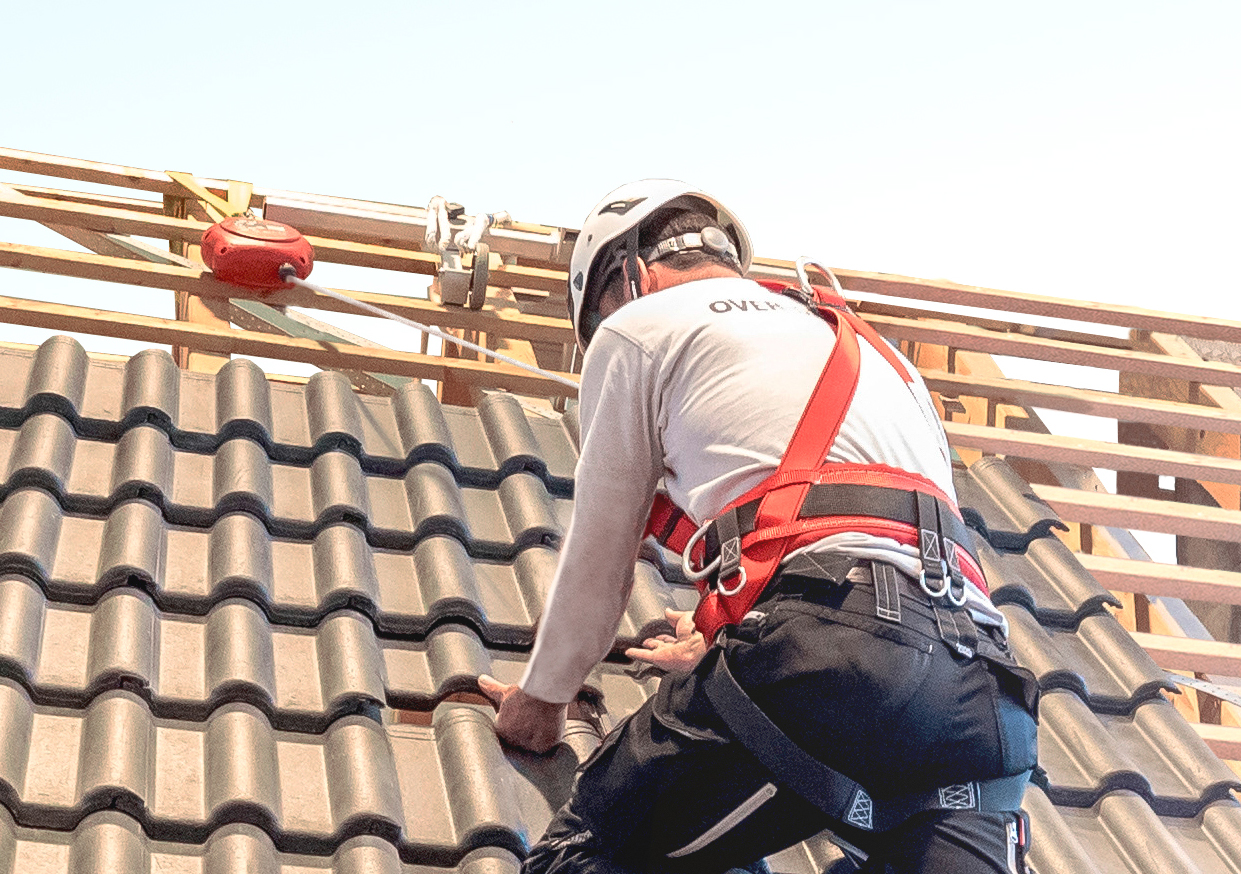 Portraitaufnahme eines Mannes, der mit PSA Schutzausrüstung auf einem Dach gesichert arbeitet.