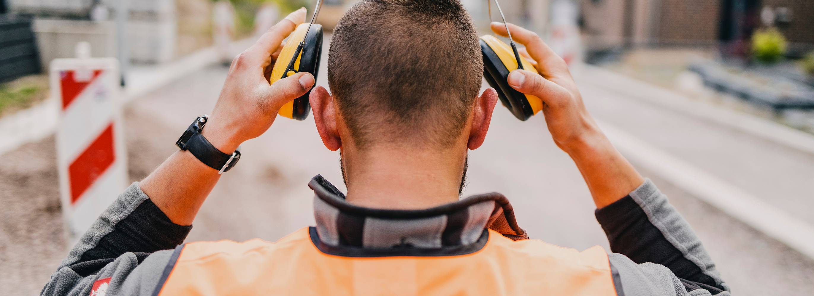 Blick auf einen Bauarbeiter von hinten, der seinen Gehörschutz aufsetzt.