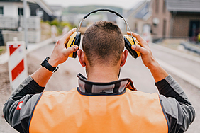 Blick auf einen Bauarbeiter von hinten, der seinen Gehörschutz aufsetzt.