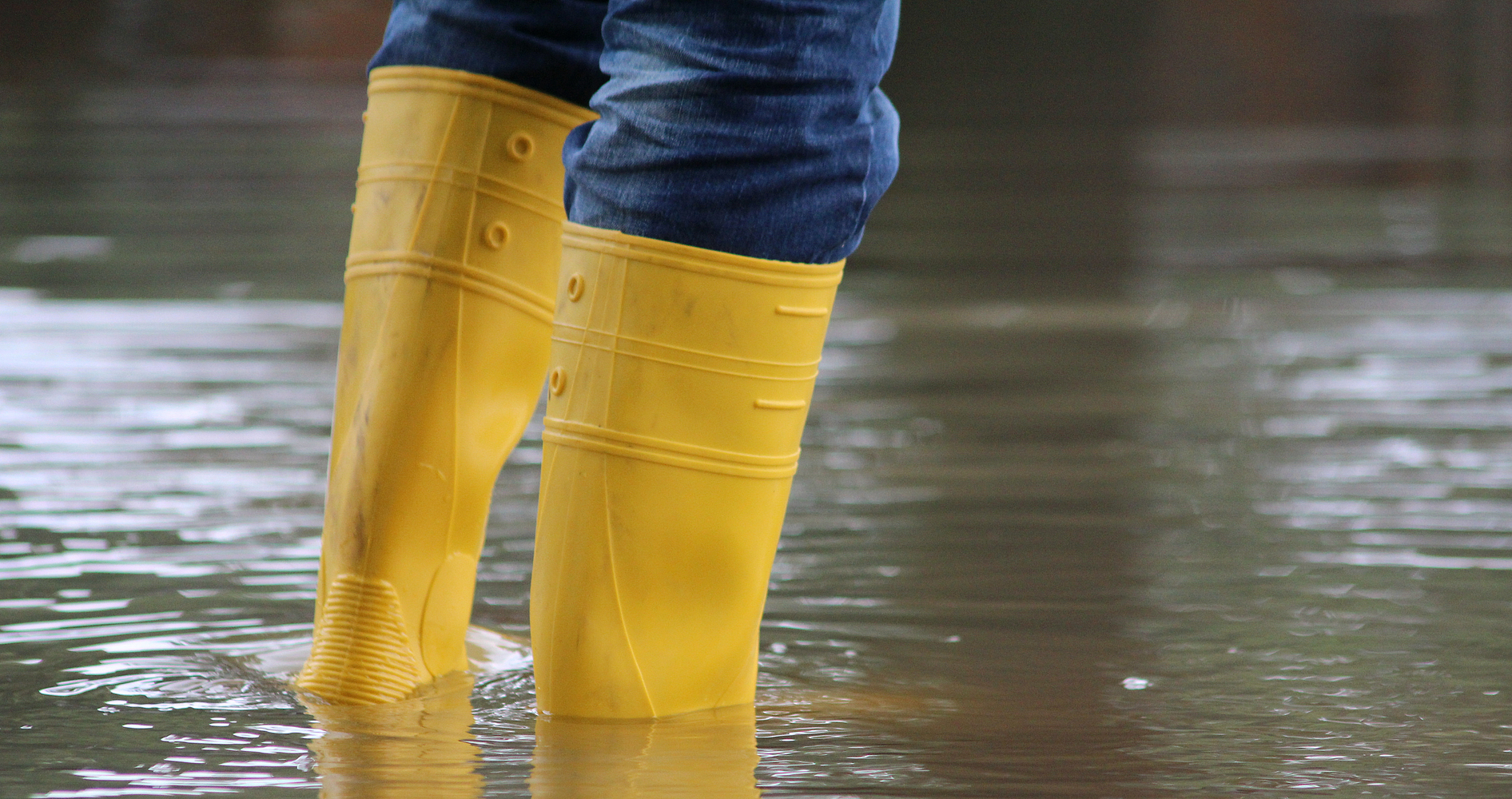 Zwei Beine mit gelben Stiefeln stehen im Hochwasser.