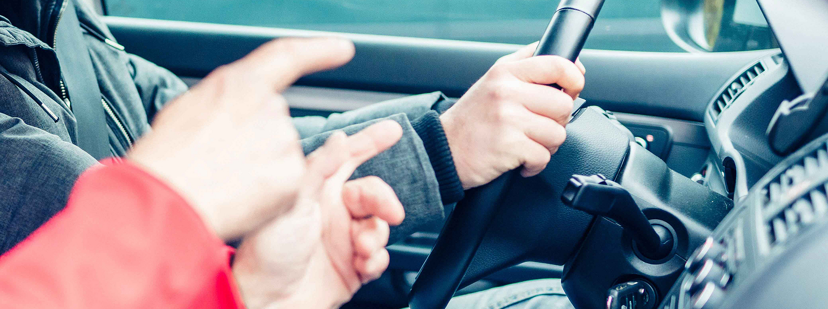 Zwei Personen, Fahrer und Beifahrer, im Auto. Der Beifahrer erzählt und zeigt dem Fahrer etwas.