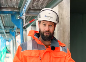 Eine Aufsichtsperson der BG BAU mit Helm steht auf einem Gerüst.