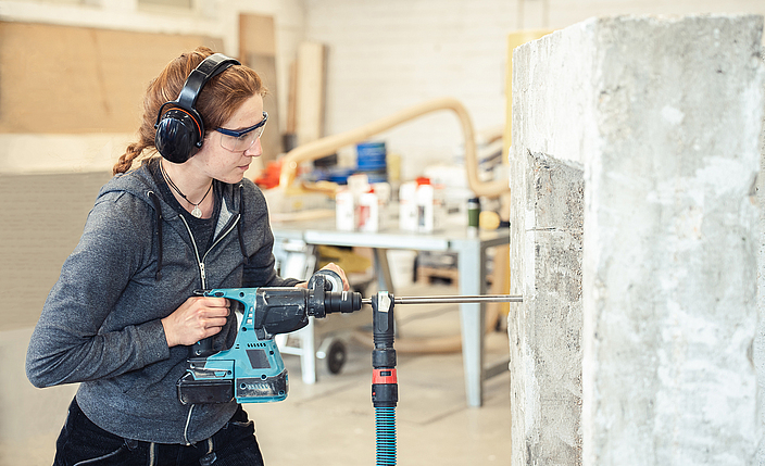 Eine Frau mit Gehörschutz bohrt mit einem Schlagbohrhammer in eine Wand.