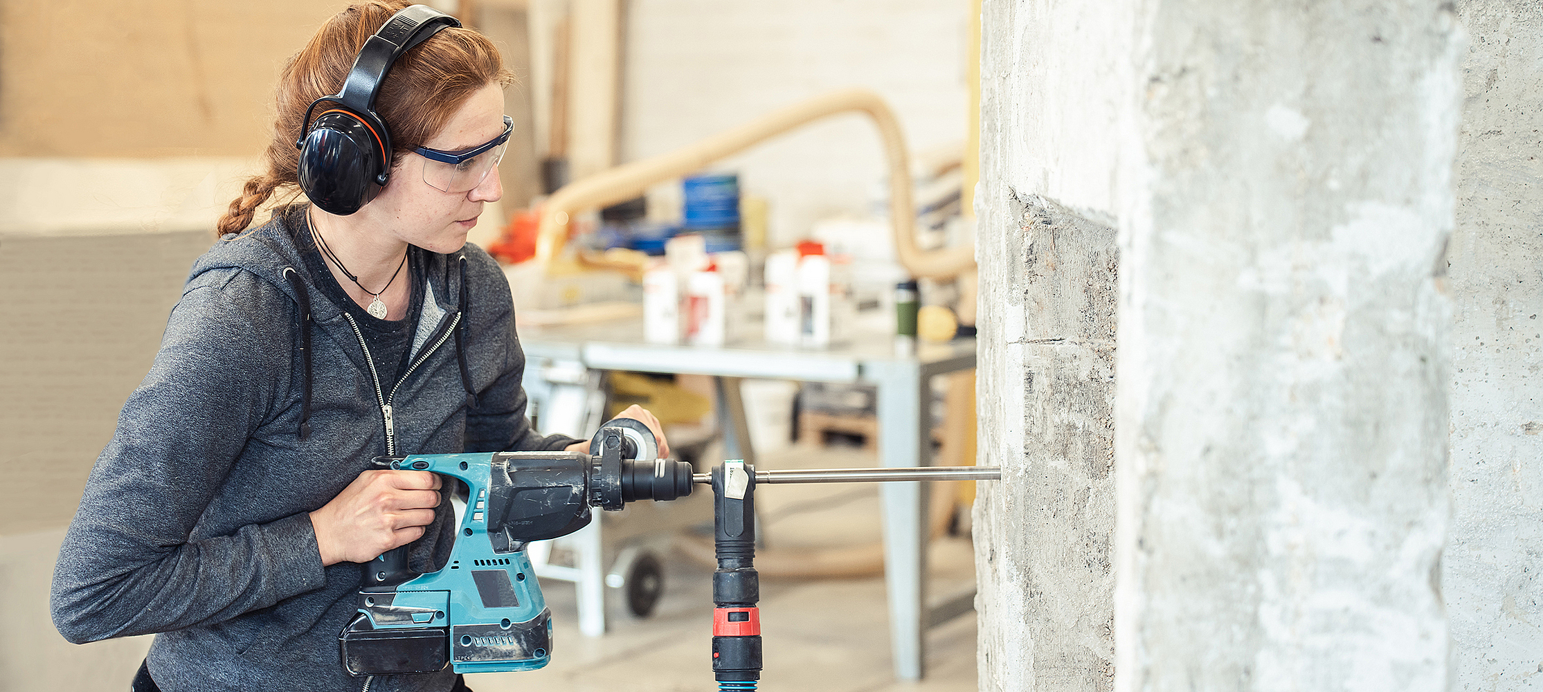 Eine Frau mit Gehörschutz bohrt mit einem Schlagbohrhammer in eine Wand.