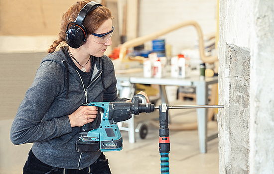 Eine Frau mit Gehörschutz bohrt mit einem Schlagbohrhammer in eine Wand.