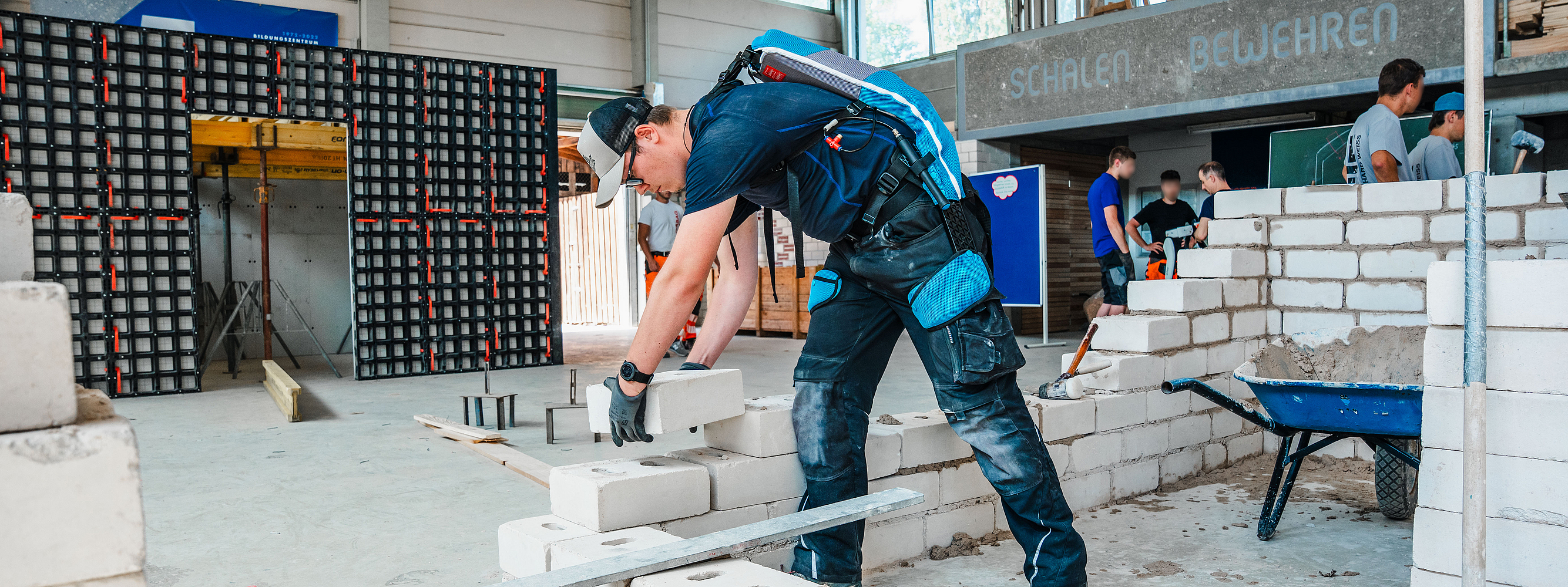 Ein Auszubildender trägt ein Exoskelett und führt in einer Halle im Bildungszentrum Bau Geradstetten Maurerarbeiten durch.
