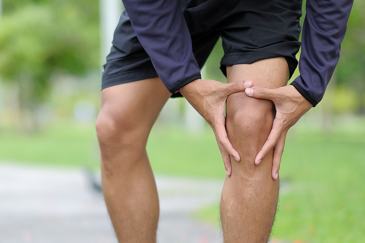 Ein Mann steht auf einem Weg und hält sein linkes Knie vor Schmerzen.