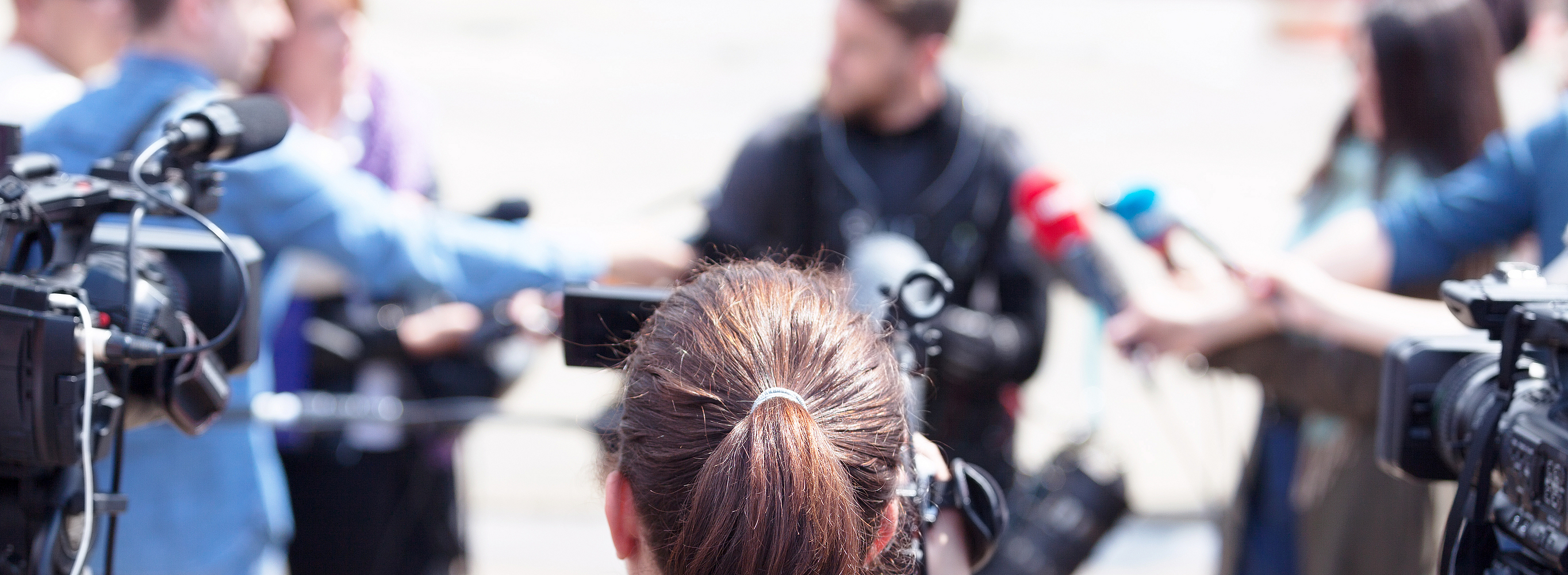 Eine Person nimmt mit einer Videokamera eine Pressekonferenz oder ein Medienereignis auf.