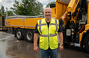 Ein Mann in Warnkleidung steht vor einer gro&szlig;en Baumaschine und l&auml;chelt in die Kamera.