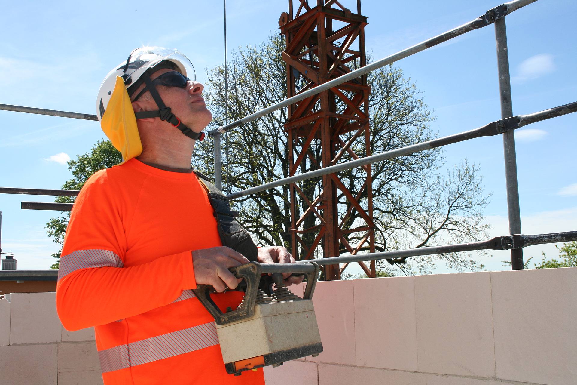 Ein Bauarbeiter trägt auf einer Baustelle UV-Schutzkleidung mit Schutzhelm, Nackenschutz und Sonnenbrille.