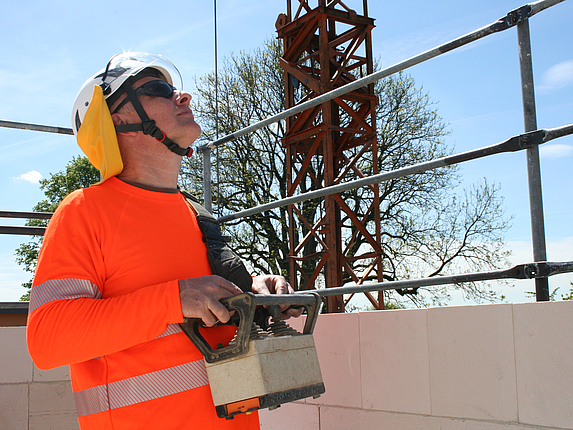 Ein Bauarbeiter auf einer Baustelle trägt UV-Schutzkleidung mit Schutzhelm, Nackenschutz und Sonnenbrille.