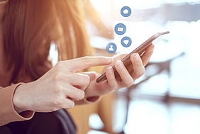 Eine Frau hat ein Handy in der Hand aus dem Icons in die Luft steigen.