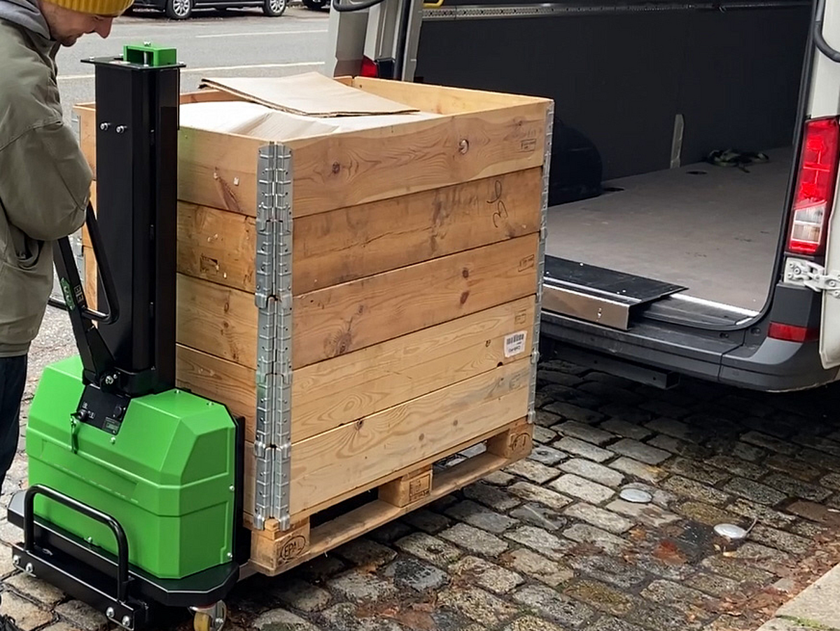 Mann schiebt einen beladenen Transportwagen zum offenen Laderaum eines Transporters.