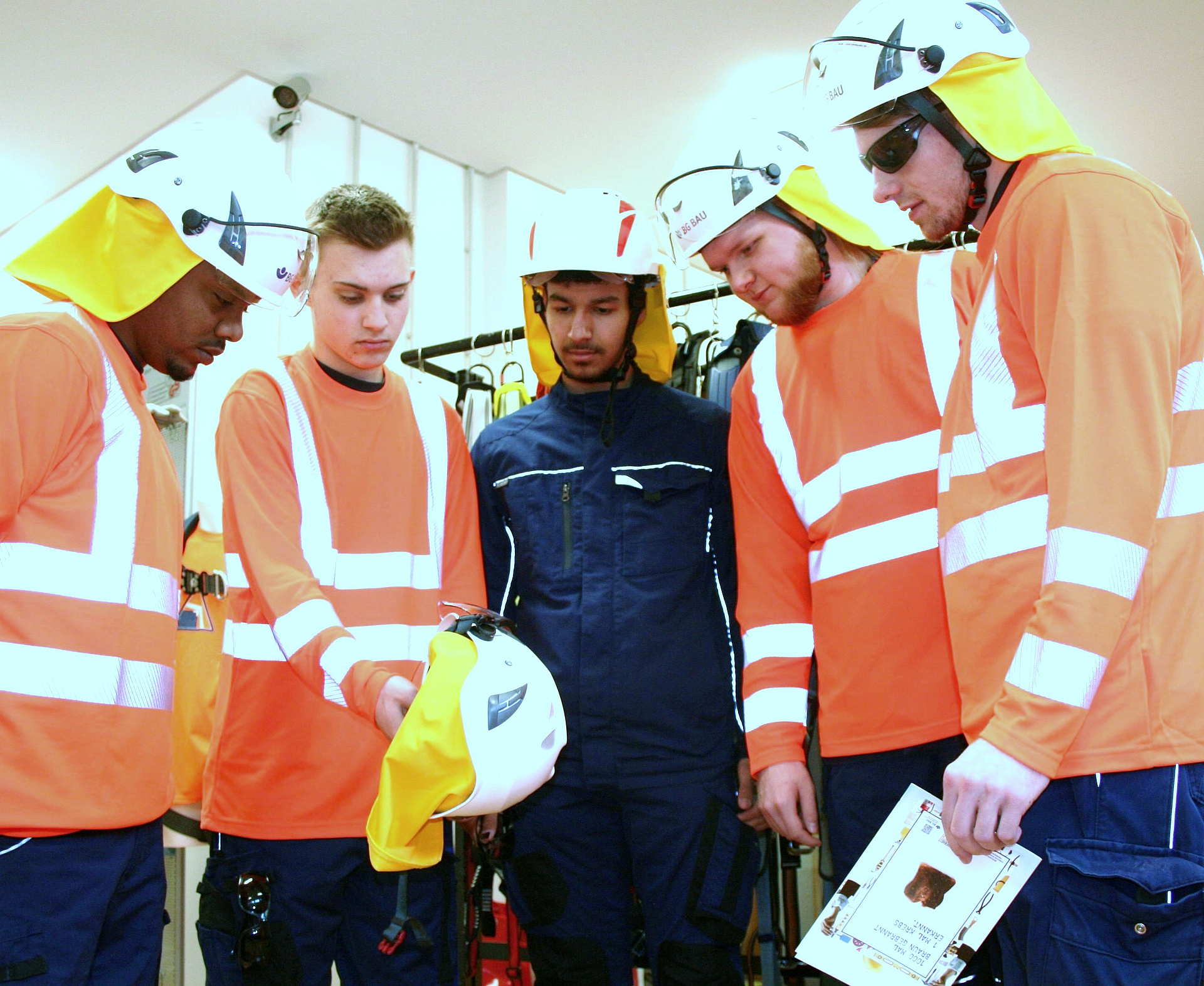 Fünf Auszubildende schauen sich einen Schutzhelm mit Nackenschutz an.