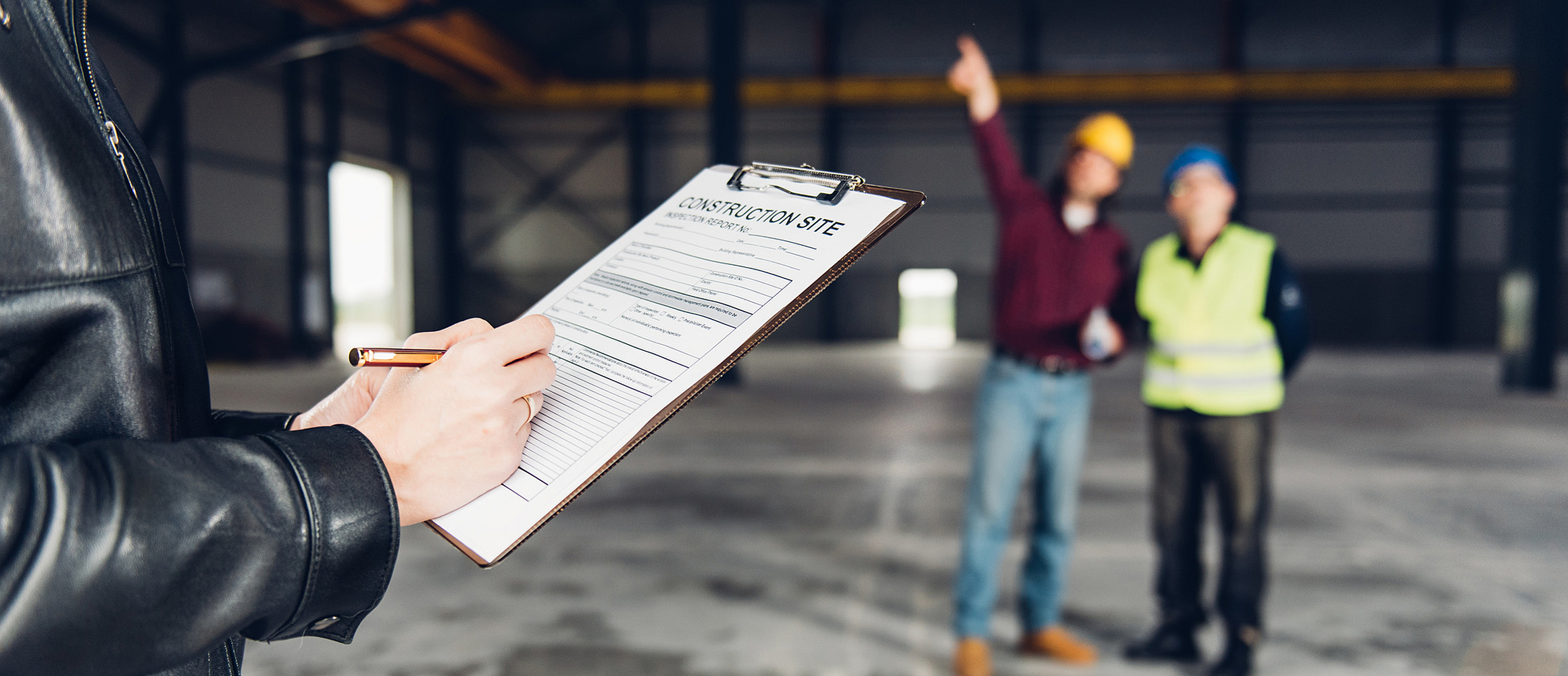 Eine Person füllt eine Gefährdungsbeurteilung aus, während ein Bauherr einer Aufsichtsperson die Baustelle zeigt