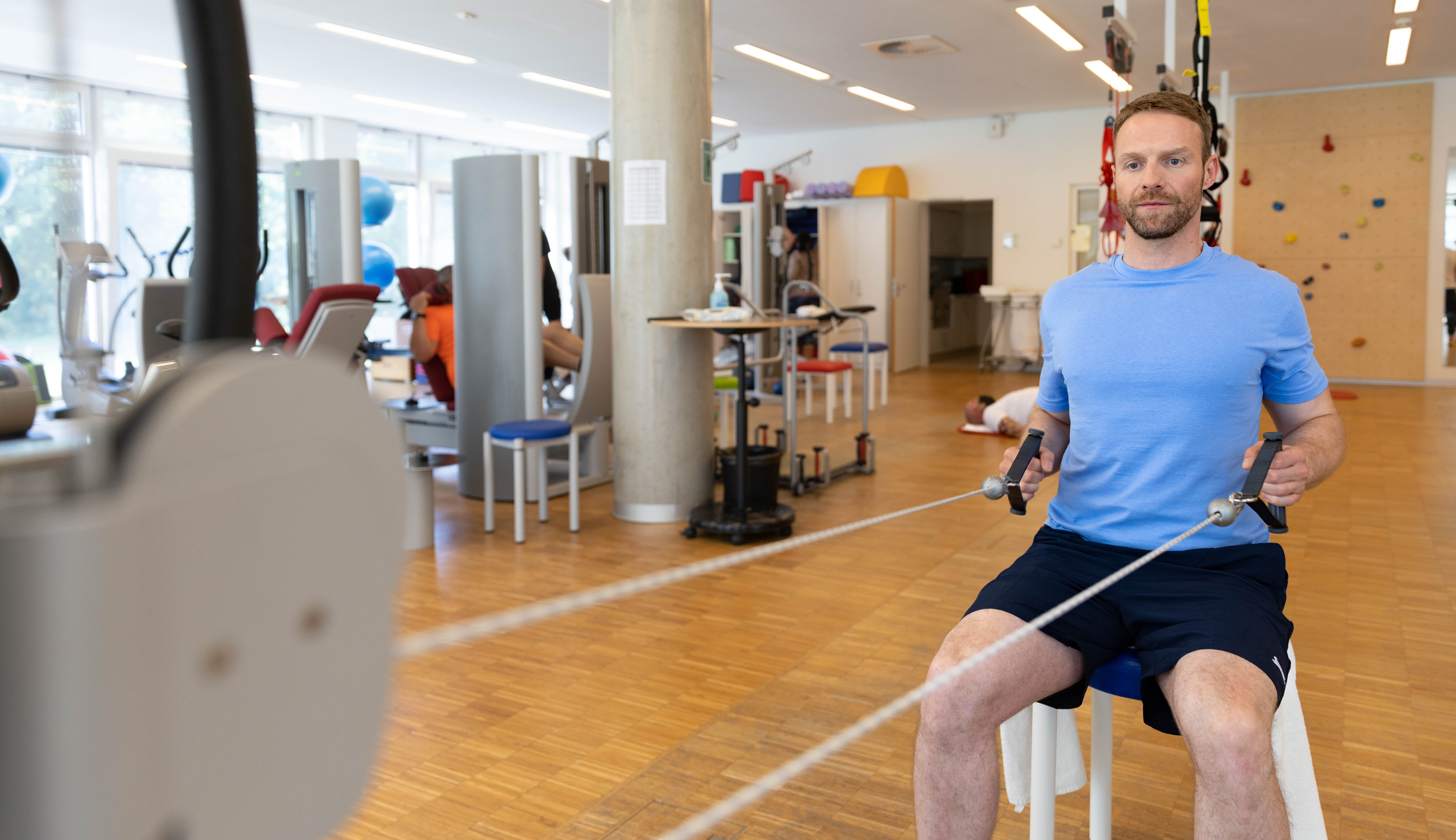 Ein Mann zieht mit beiden H&auml;nden an den Seilen eines Kabelzug-Ger&auml;ts.