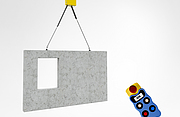 Ein Balancer hebt eine große vorgefertigte Betonwand mit rechteckiger Öffnung an zwei Ketten an. Rechts im Bild schwebt eine kabellose Steuerung mit Drucktasten und Display.
