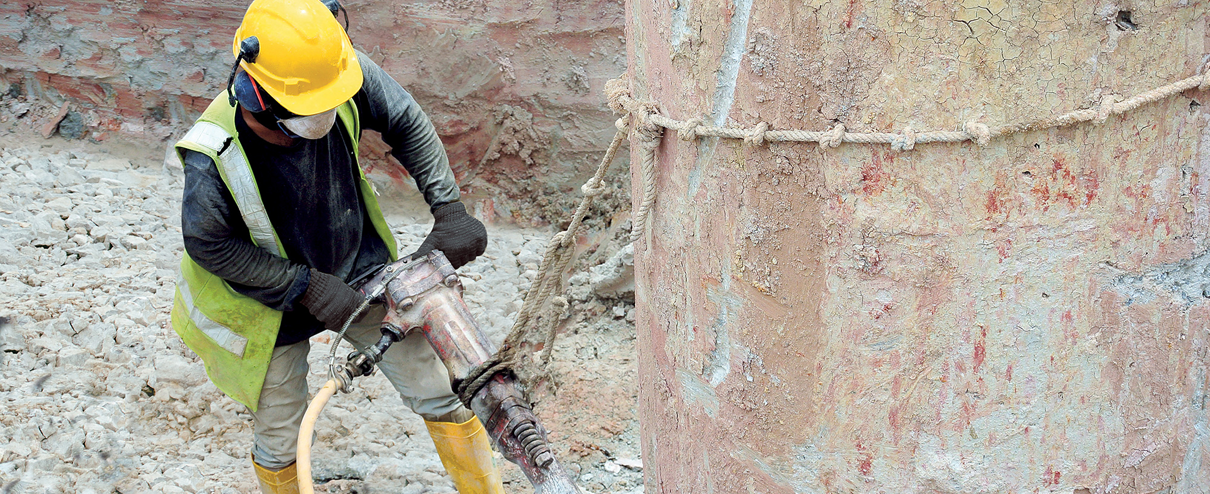 Ein Arbeiter steht in einer Baugrube und hat einen Presslufthammer in der Hand.
