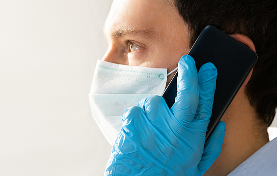 Ein Mann mit medizinischer OP-Maske am Telefon.