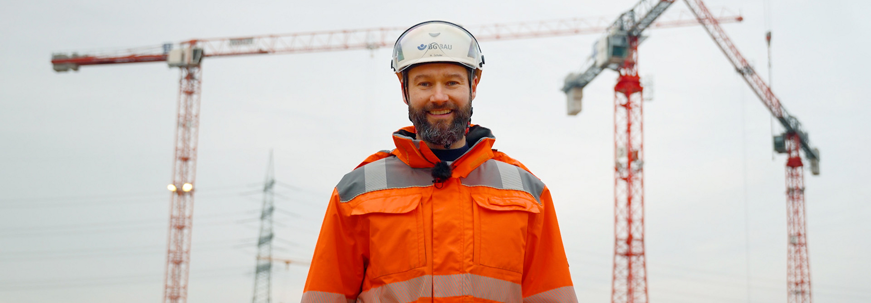 Titelbild des Videos "9 lebenswichtige Regeln im Hochbau": Marc Schuler steht auf einer Baustelle vor drei Kränen.