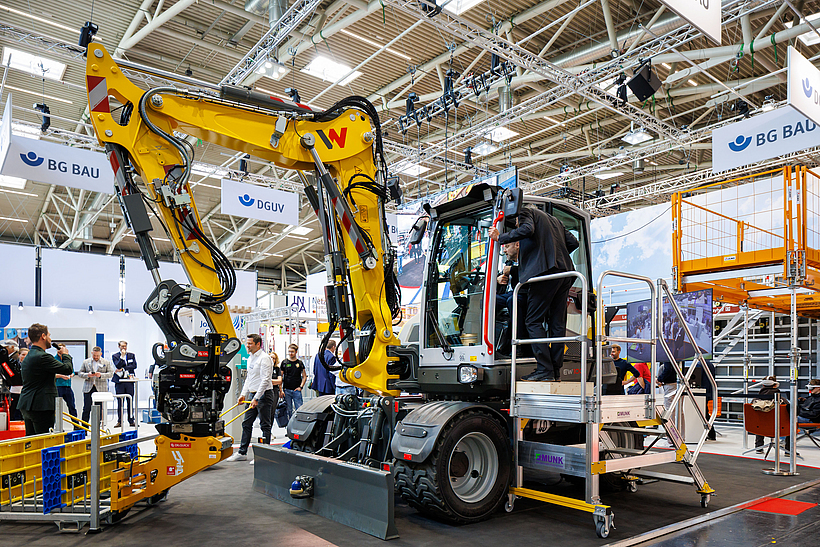 Bagger, der mit einem KI-gestützten Assistenzsystem ausgestattet ist, am bauma-Messestand der BG BAU.