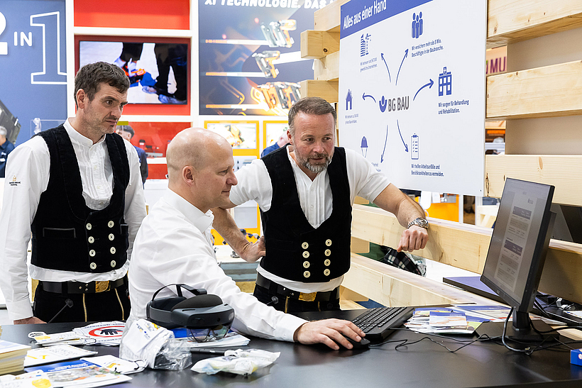 Ein Messebetreuer im Austausch mit zwei Zimmerern. Er zeigt ihnen ein Dokument auf dem Monitor.