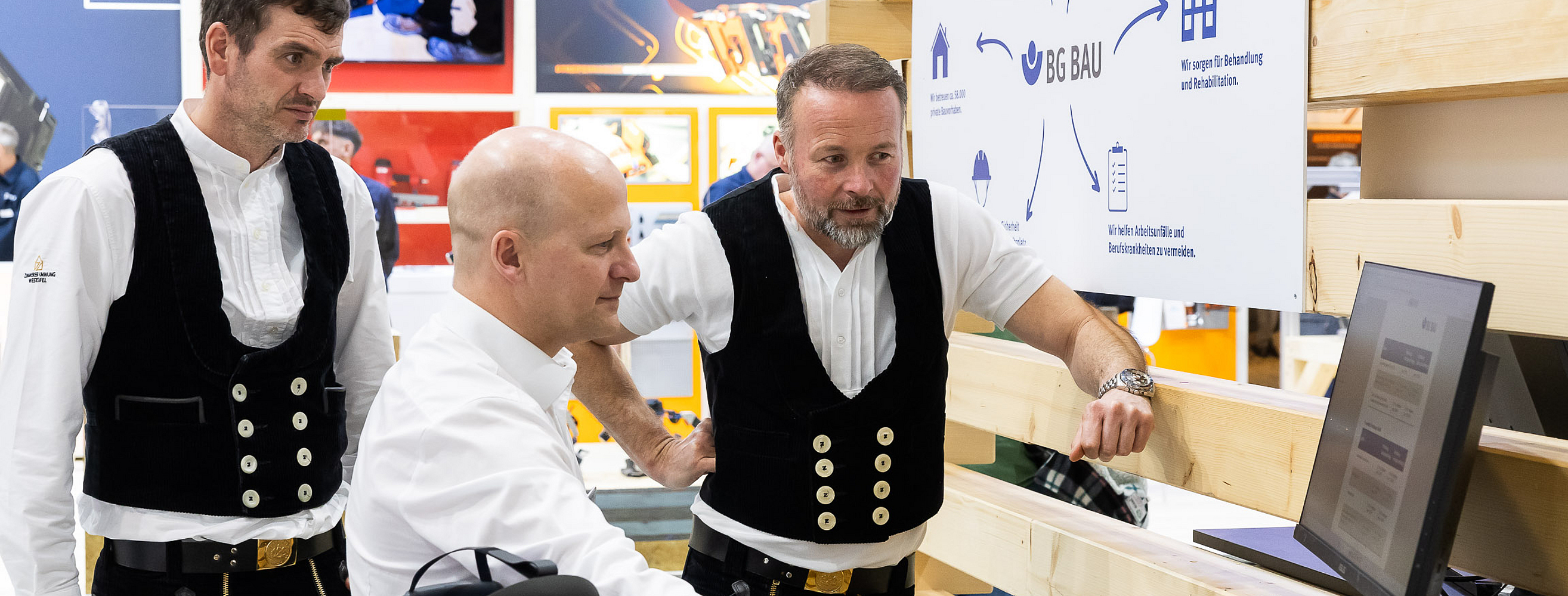 Ein Messebetreuer im Austausch mit zwei Zimmerern. Er zeigt ihnen ein Dokument auf dem Monitor.