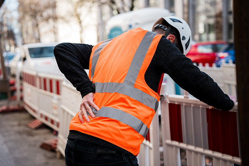 Das Foto zeigt einen Bauarbeiter, der sich an den schmerzenden R&uuml;cken fasst. 