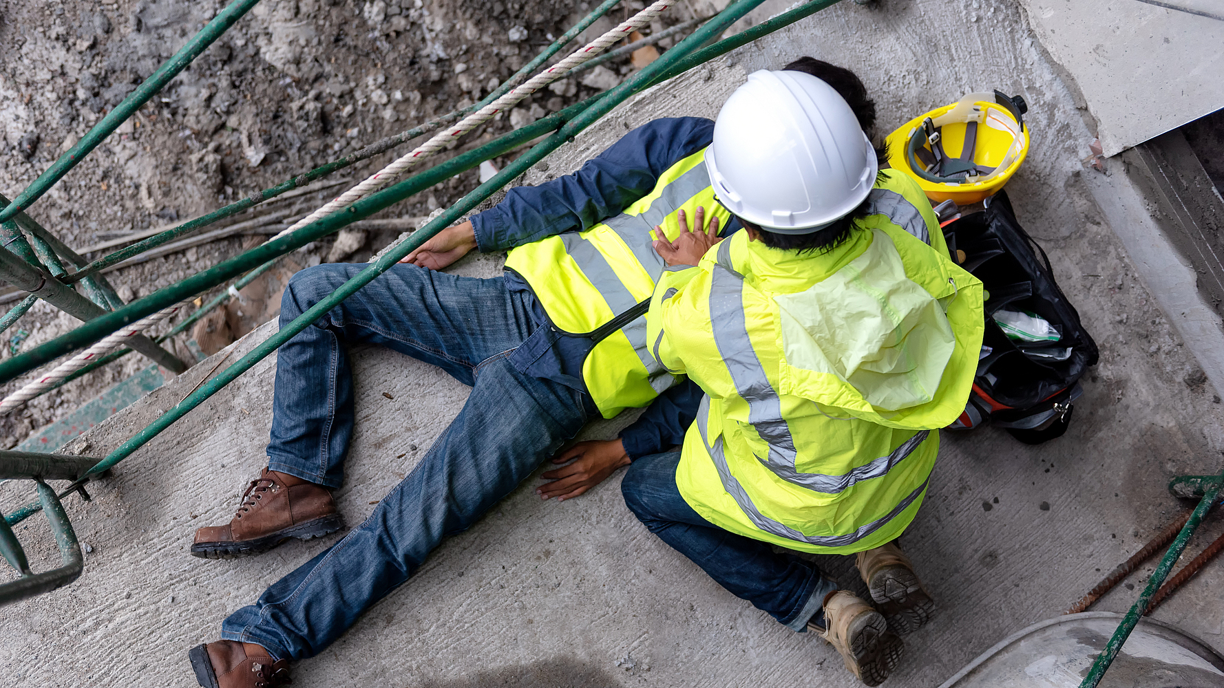 Ein Bauarbeiter hat einen Arbeitsunfall. Ein anderer Bauarbeiter leistet Erste-Hilfe.