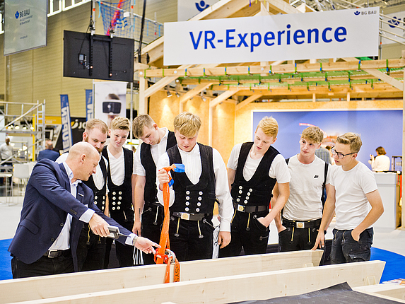 Eine Person präsentiert Interessierten auf einer Messe den Einsatz eines ferngesteuerten Automatikhakens.