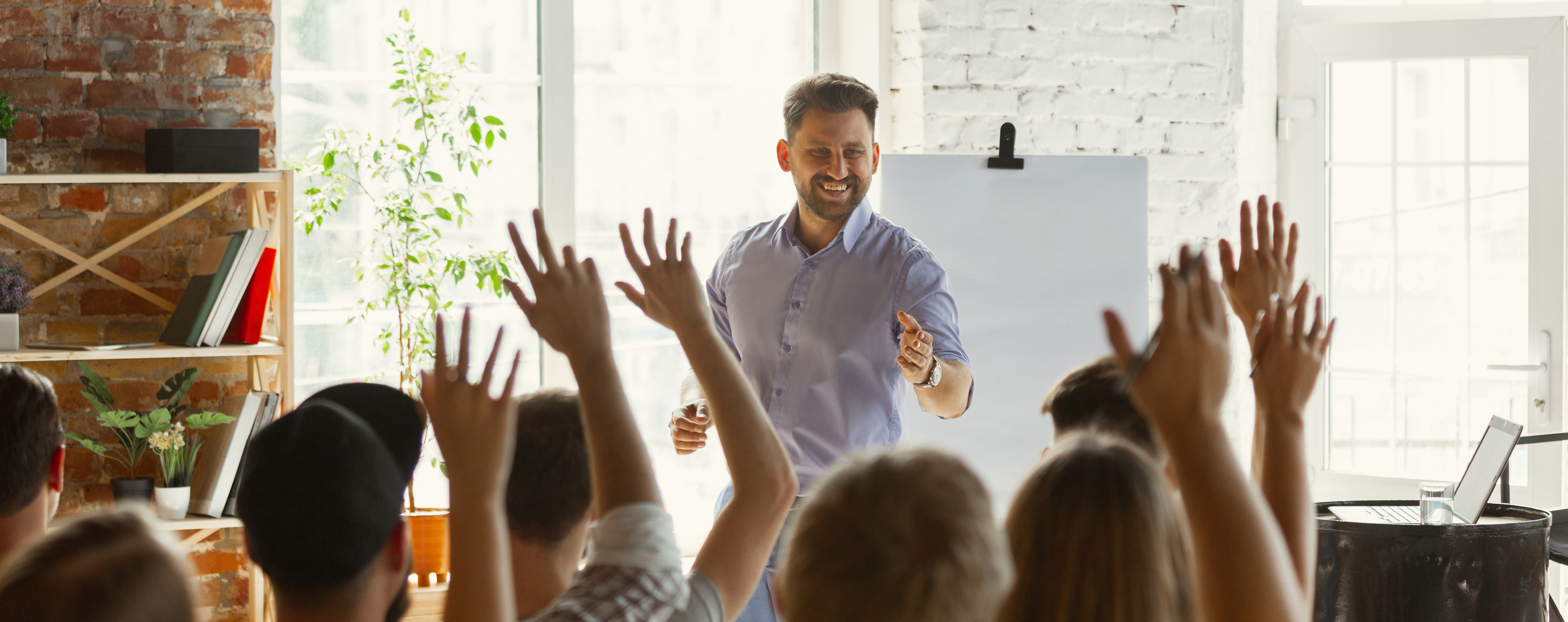 Ein Dozent an einem Flipchart zeigt mit der Hand auf einen Teilnehmer. Mehrere Teilnehmende melden sich.