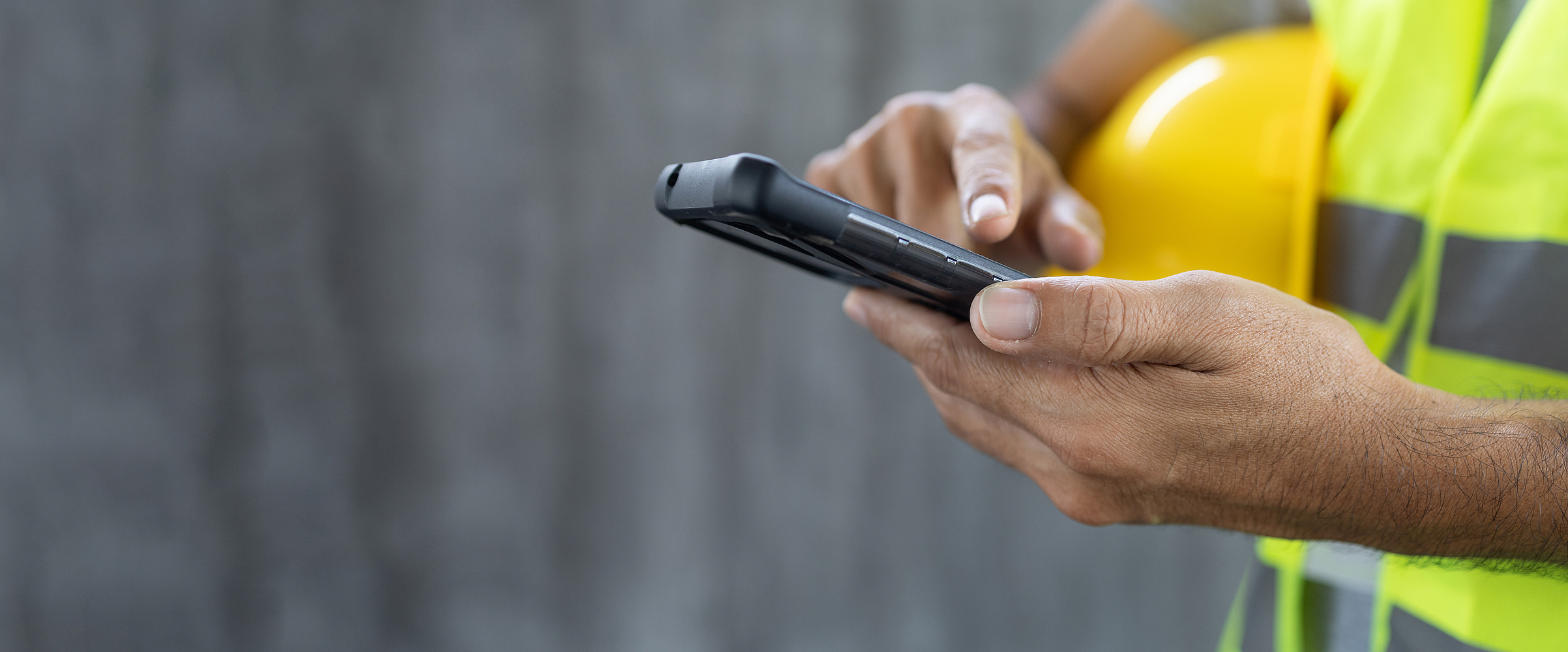Finger eines Bauarbeiters tippt auf einem Smartphone.