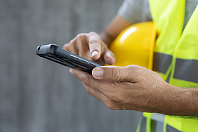 Finger eines Bauarbeiters tippt auf einem Smartphone.
