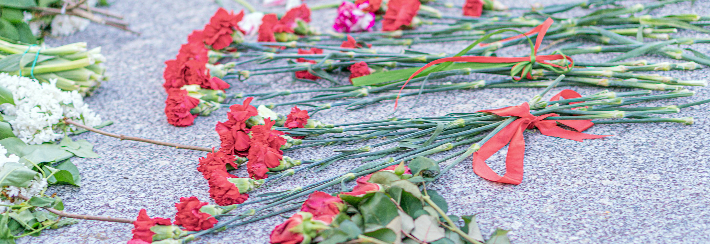 Rote Nelken und andere Blumen liegen zu kleinen Sträußen gebunden nebeneinander auf dem Steinboden.