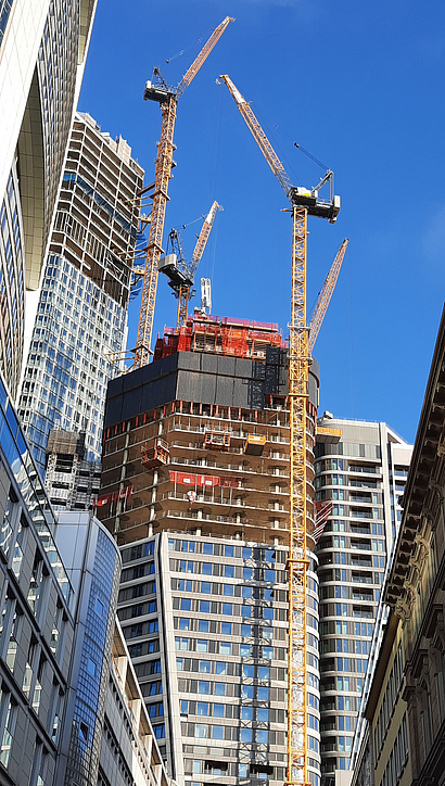 Mehrere Kräne stehen um ein Baustellen an einem Hochhaus.
