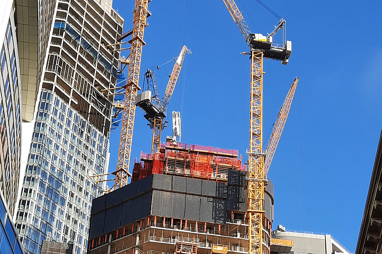 Mehrere Kräne stehen um ein Baustellen an einem Hochhaus.