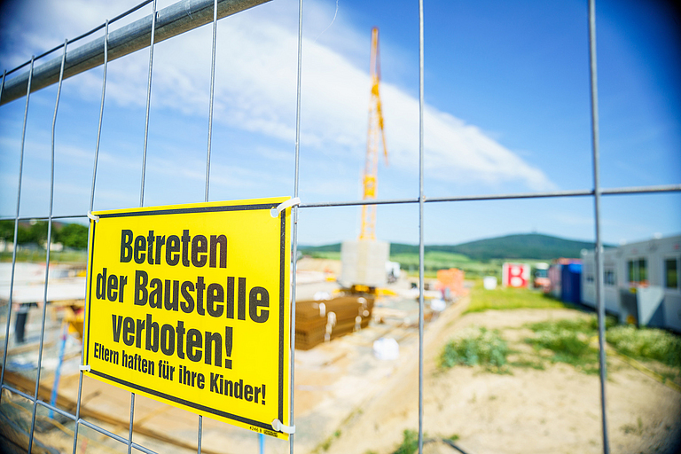 Gelände einer Baustelle mit gelben Schild am Zaun: Betreten der Baustelle verboten! Eltern haften für ihre Kinder!