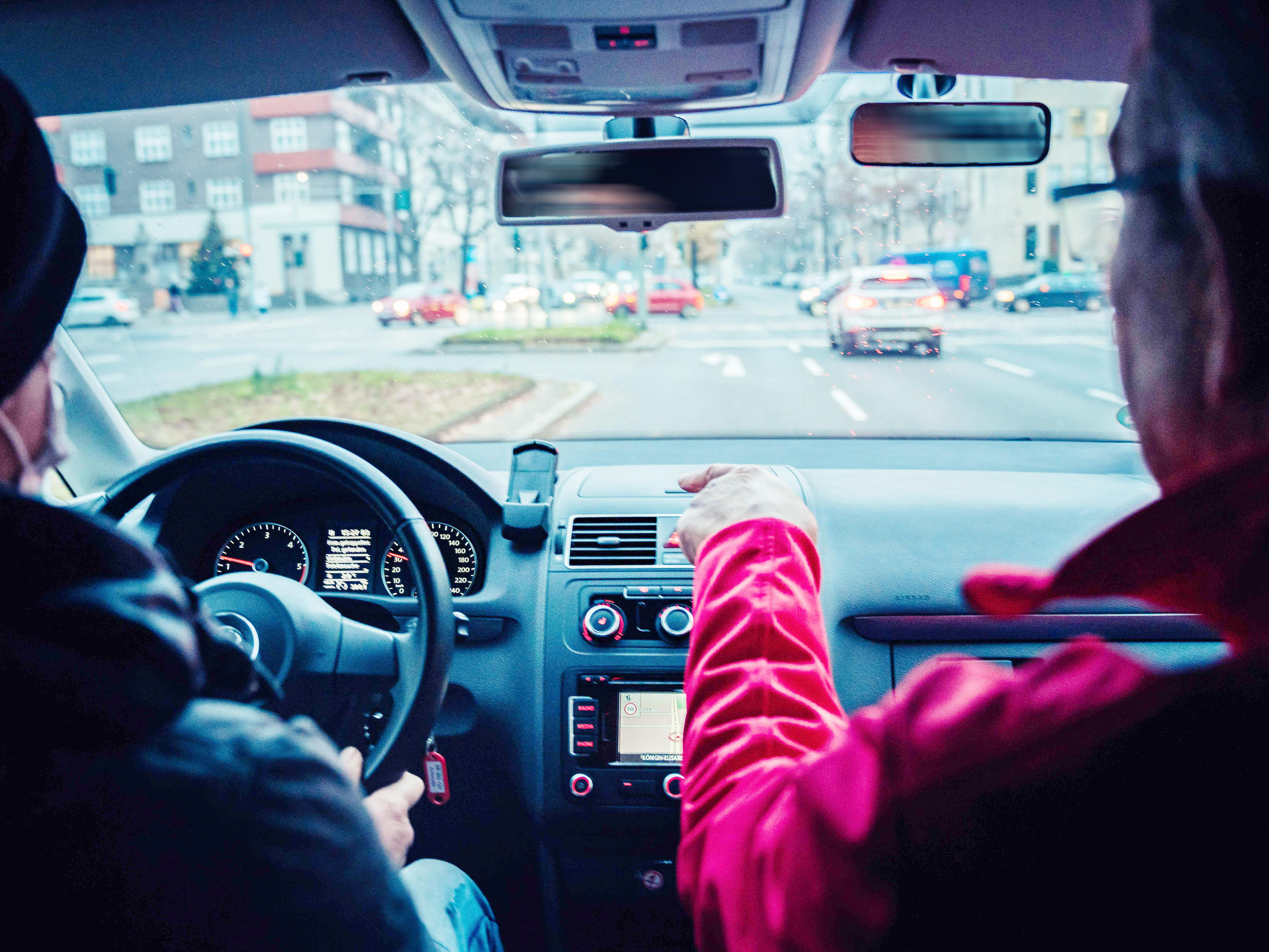 Zwei Personen, Autofahrer und Beifahrer, sitzen in einem Auto und schauen auf den Verkehr.