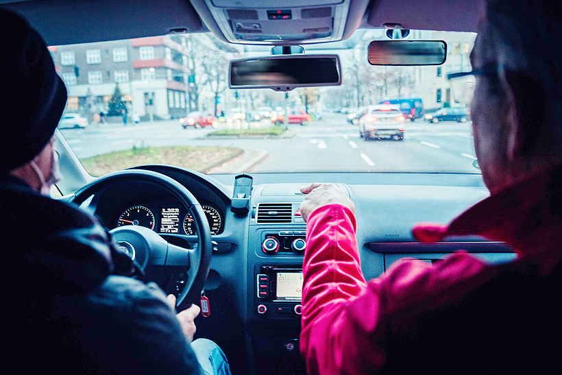 Zwei Personen, Autofahrer und Beifahrer, sitzen in einem Auto und schauen auf den Verkehr.