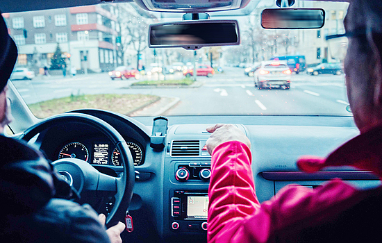 Zwei Personen, Autofahrer und Beifahrer, sitzen in einem Auto und schauen auf den Verkehr.