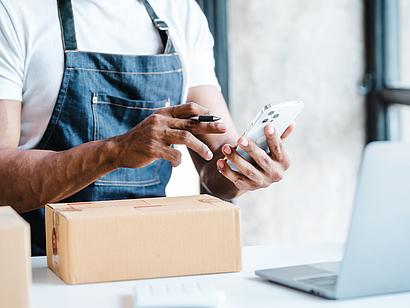 Ein Mann überprüft und stellt Paket-Bestellungen zusammen mit einem Smartphone und einem Laptop.
