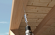 Eine Einschraubhilfe stabilisiert eine lange Holzbauschraube, die mit einem Akkuschrauber senkrecht in eine Holzdecke eingedreht wird.