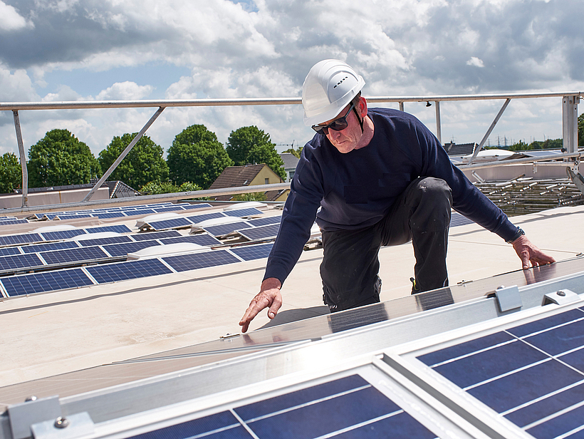 Ein Bauarbeiter mit Schutzhelm arbeitet an einer Photovoltaikanlage auf einem Dach.