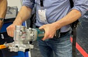 Eine Person hält einen akkubetriebenen Bewehrungsstahlschneider mit beiden Händen und präsentiert das Werkzeug auf einer Messe.