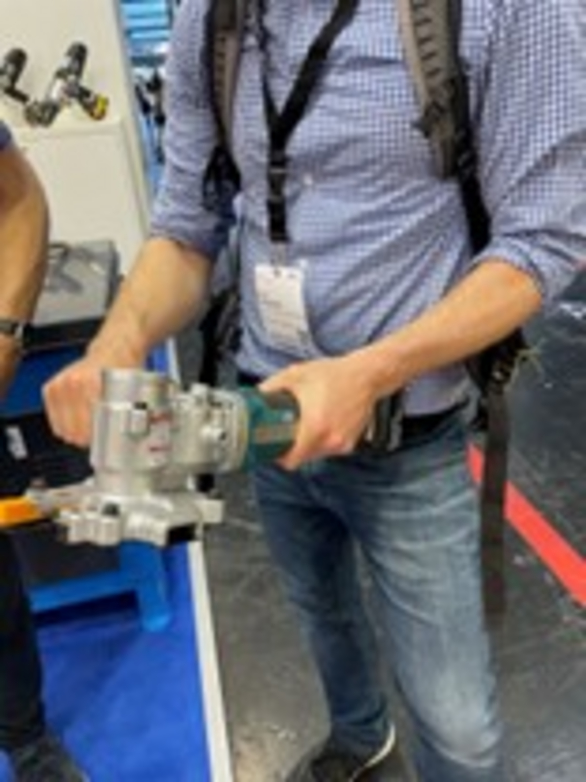 Eine Person hält einen akkubetriebenen Bewehrungsstahlschneider mit beiden Händen und präsentiert das Werkzeug auf einer Messe.