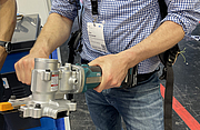 Eine Person hält einen akkubetriebenen Bewehrungsstahlschneider mit beiden Händen und präsentiert das Werkzeug auf einer Messe.