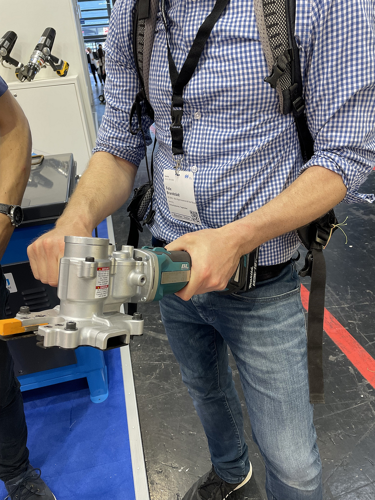 Eine Person hält einen akkubetriebenen Bewehrungsstahlschneider mit beiden Händen und präsentiert das Werkzeug auf einer Messe.