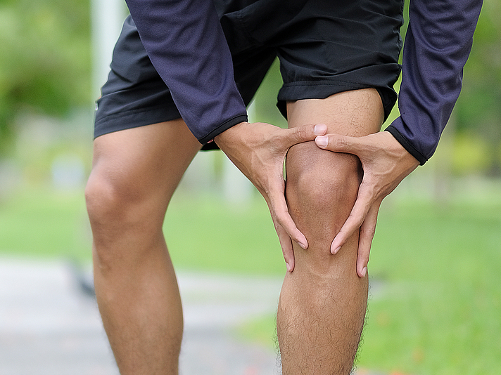 Ein Mann steht auf einem Weg und hält sein linkes Knie vor Schmerzen.